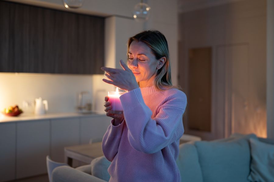 A woman smelling a scented candle in her house.